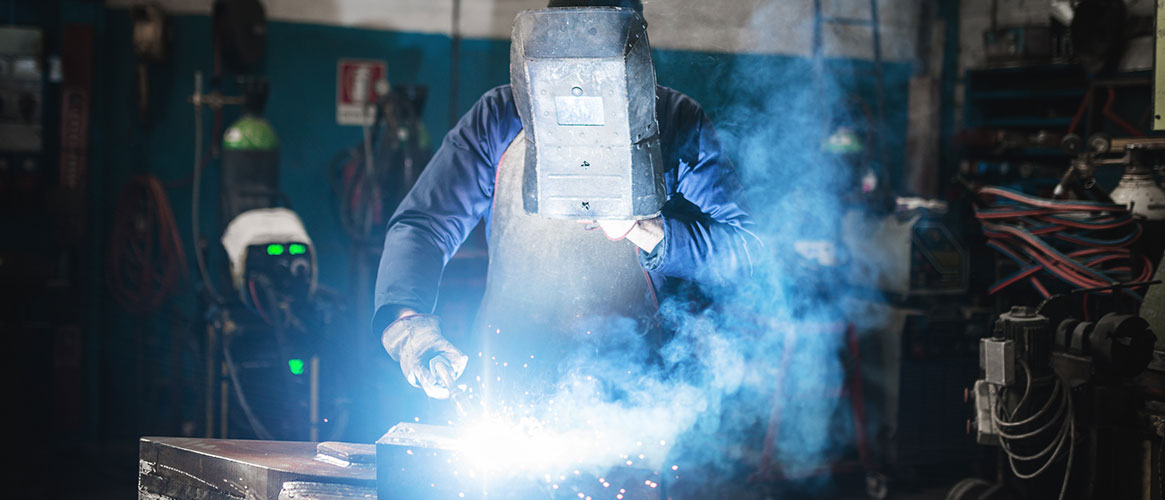 A welder wearing safety gear welds two pieces of metal as sparks fly in all directions