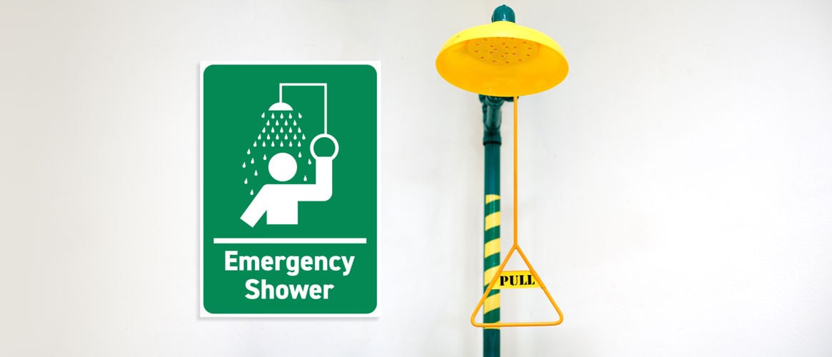 An emergency shower with the activation handle next to a sign that identifies it.