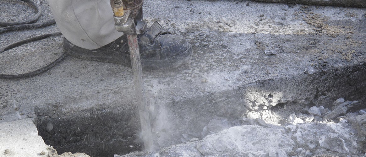 Worker using a jackhammer on concrete at a construction site