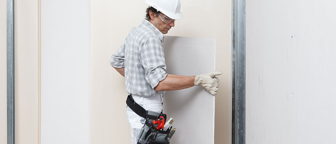 Worker handling a sheet of drywall during construction of a home.