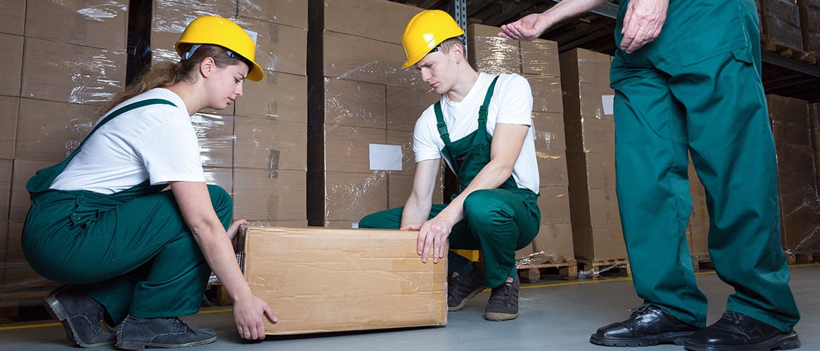 Two young workers lifting heavy box in warehouse